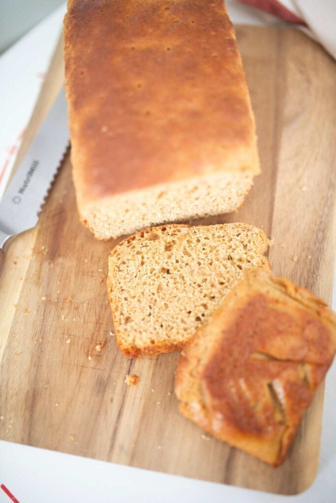 An overhead photo of a loaf of bread with 2 slices laying in front of it on a cutting board.