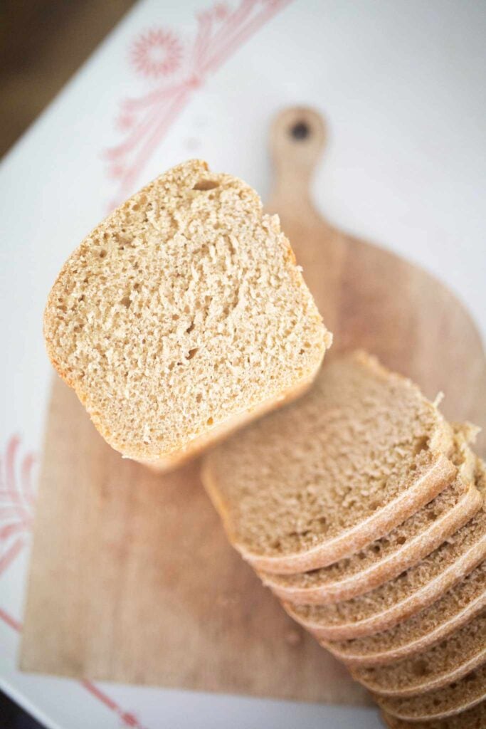Half a loaf of bread is laying crumb side up on a cutting board with several slices laid out in front of it.