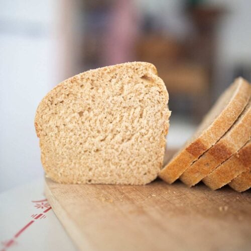 A half of a loaf of sandwich bread is on a cutting board to show crumb and there are some slices beside it.