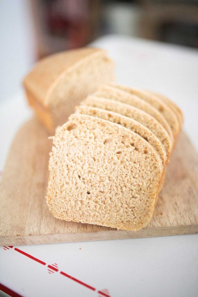 Slices of a loaf of sandwich bread are cascading on a wooden cutting board.