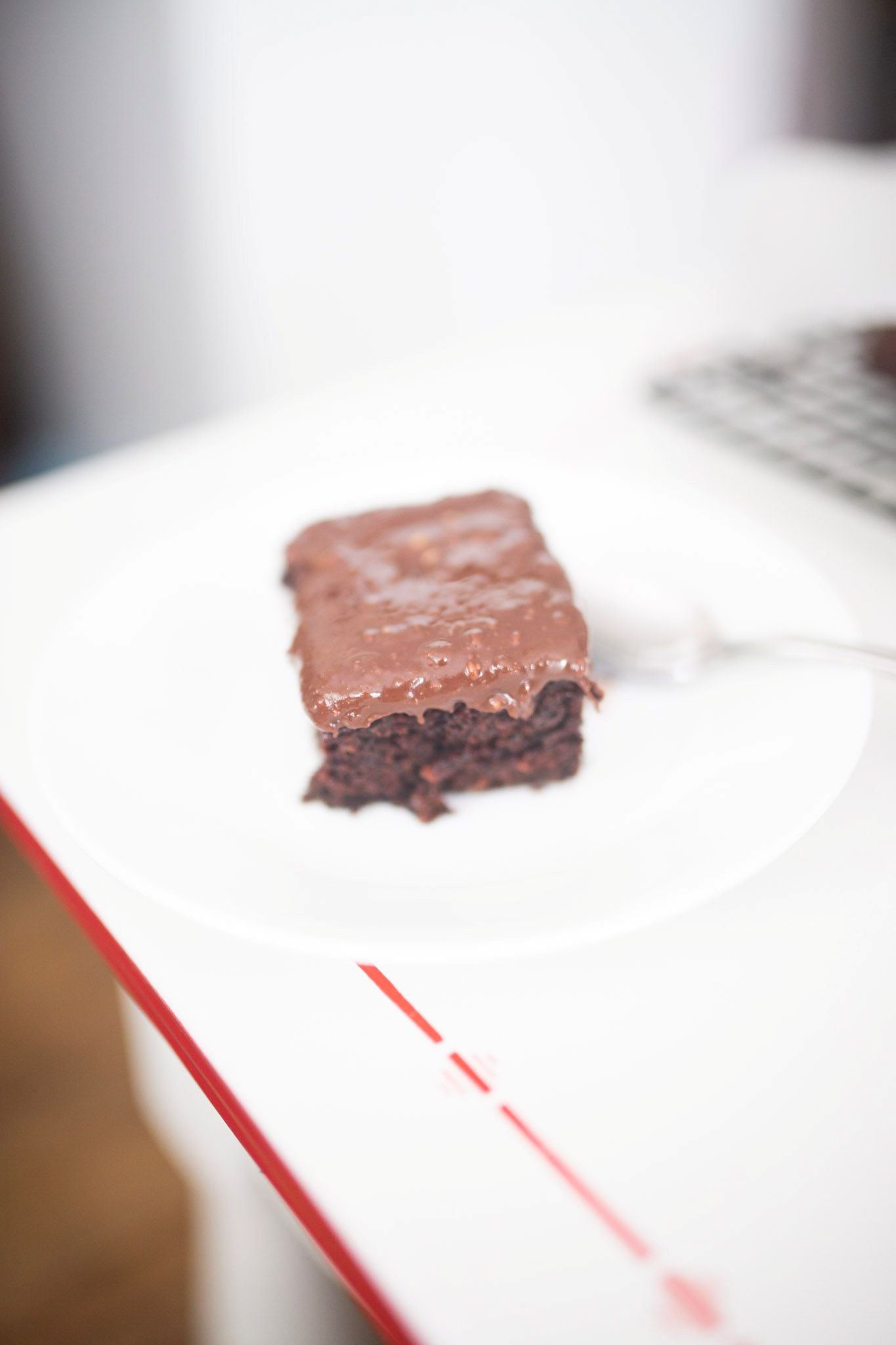 A slice of chocolate cake sits on a white plate with a spoon