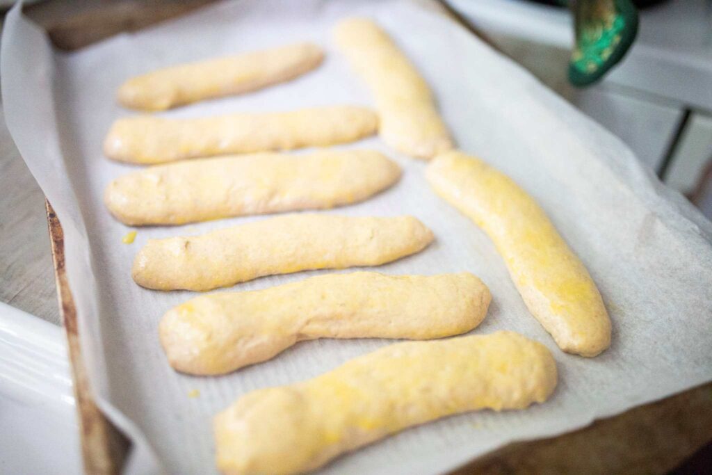 There are shaped hot dog buns on a baking sheet topped with an egg wash.