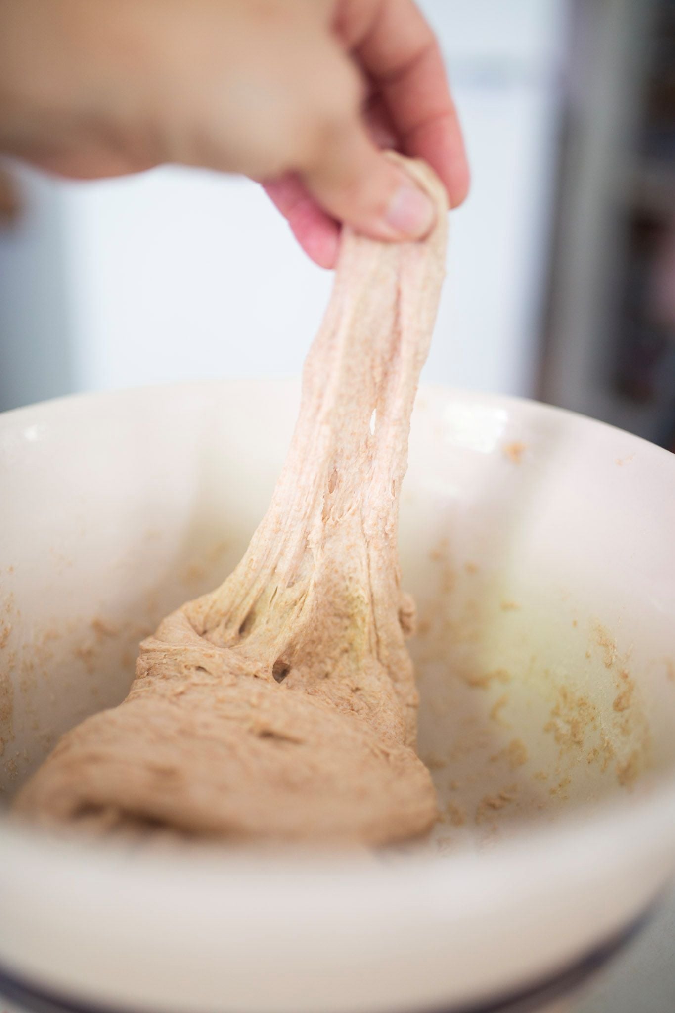 There is a hand stretching dough that is in a cream colored bowl.