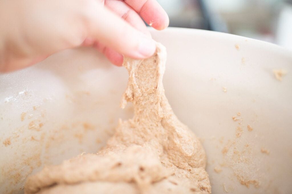 There is a hand stretching dough that is tearing while being stretched.