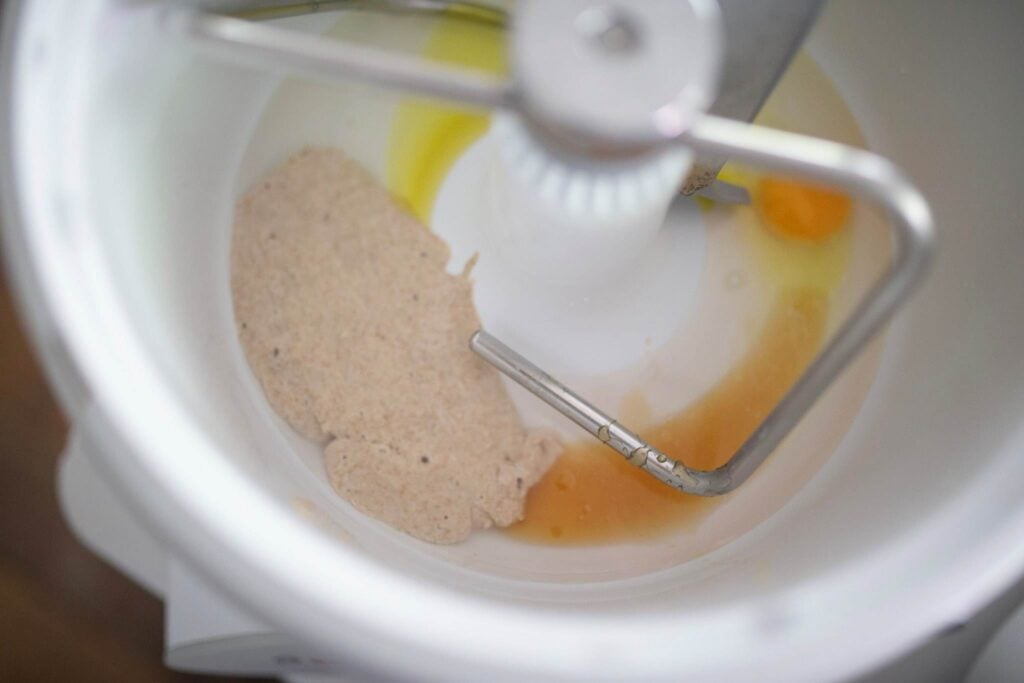 There are wet ingredients in a stand mixer with a dough hook.