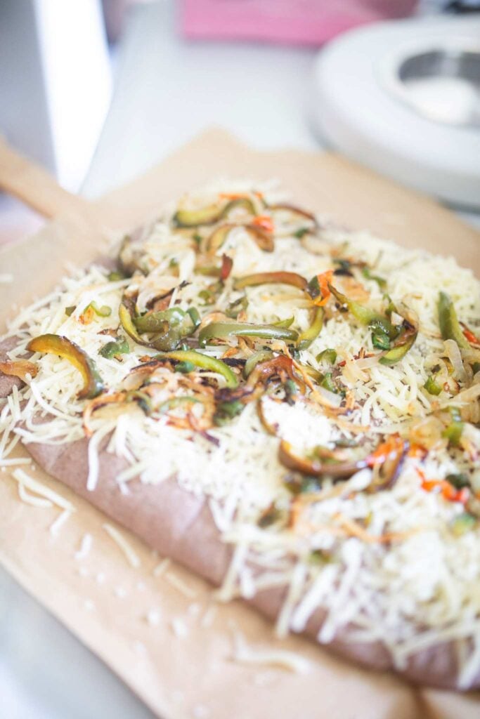 Breadsticks topped with cheese and veggies before broiling.