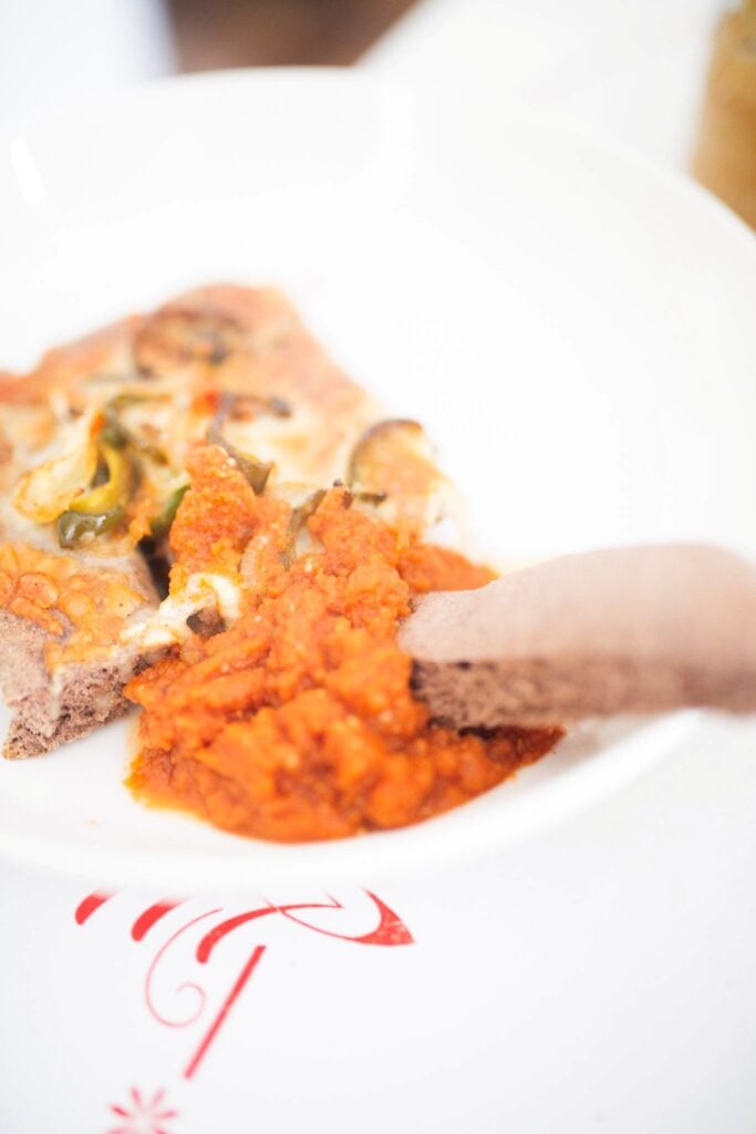 A breadstick is dipped in a red sauce on a white plate.