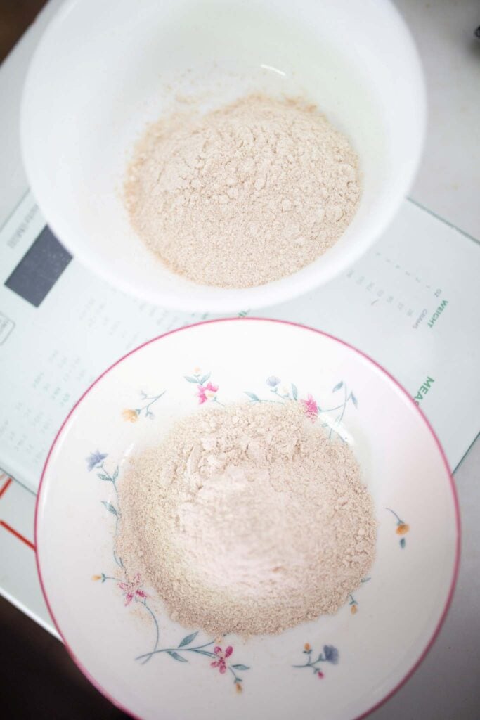 There are 2 small bowls sitting on a kitchen scale with a mound of flour in each.