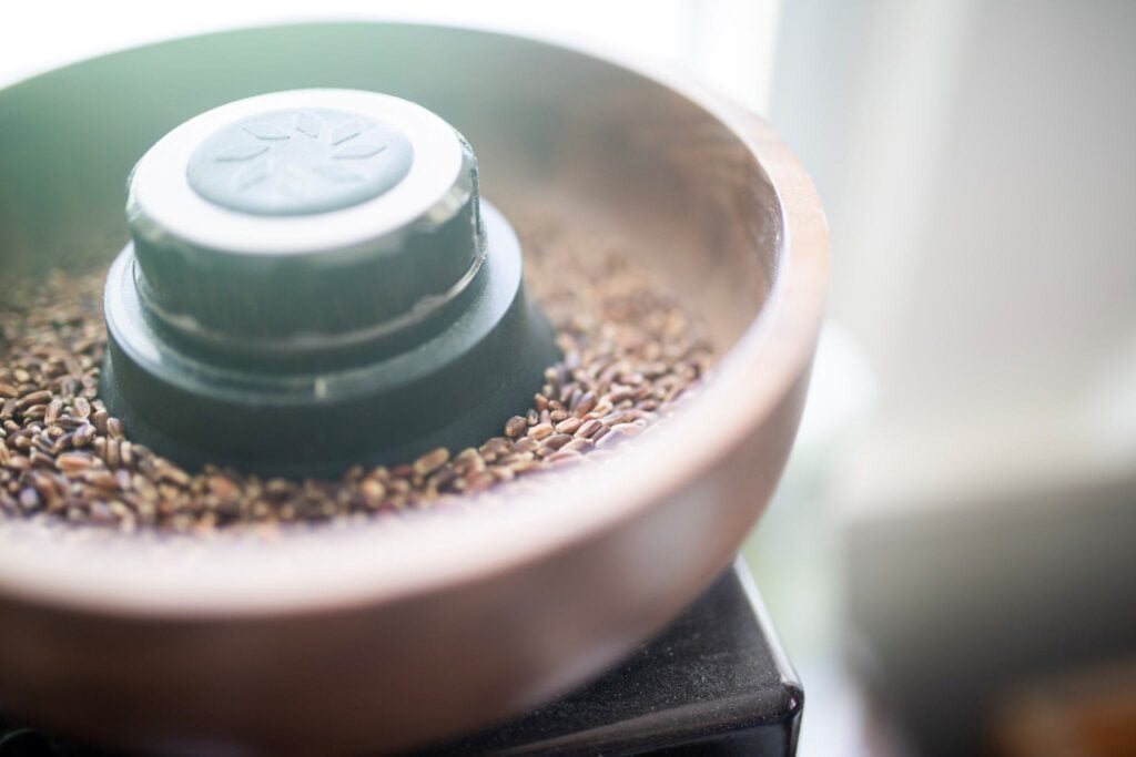 There are purple wheat berries in the hopper of a wooden grain mill.