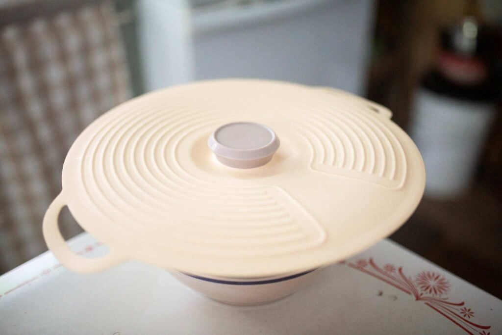 A mixing bowl is topped with a coral colored silicone lid.