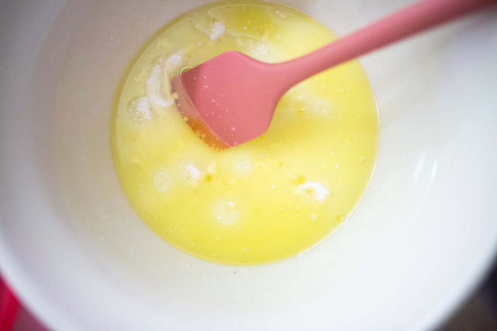 Liquid ingredients in a bowl with a pink spatula.
