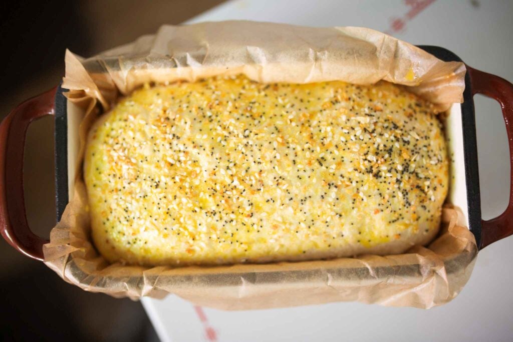 Sandwich bread dough in loaf pan topped with egg wash and seeds.