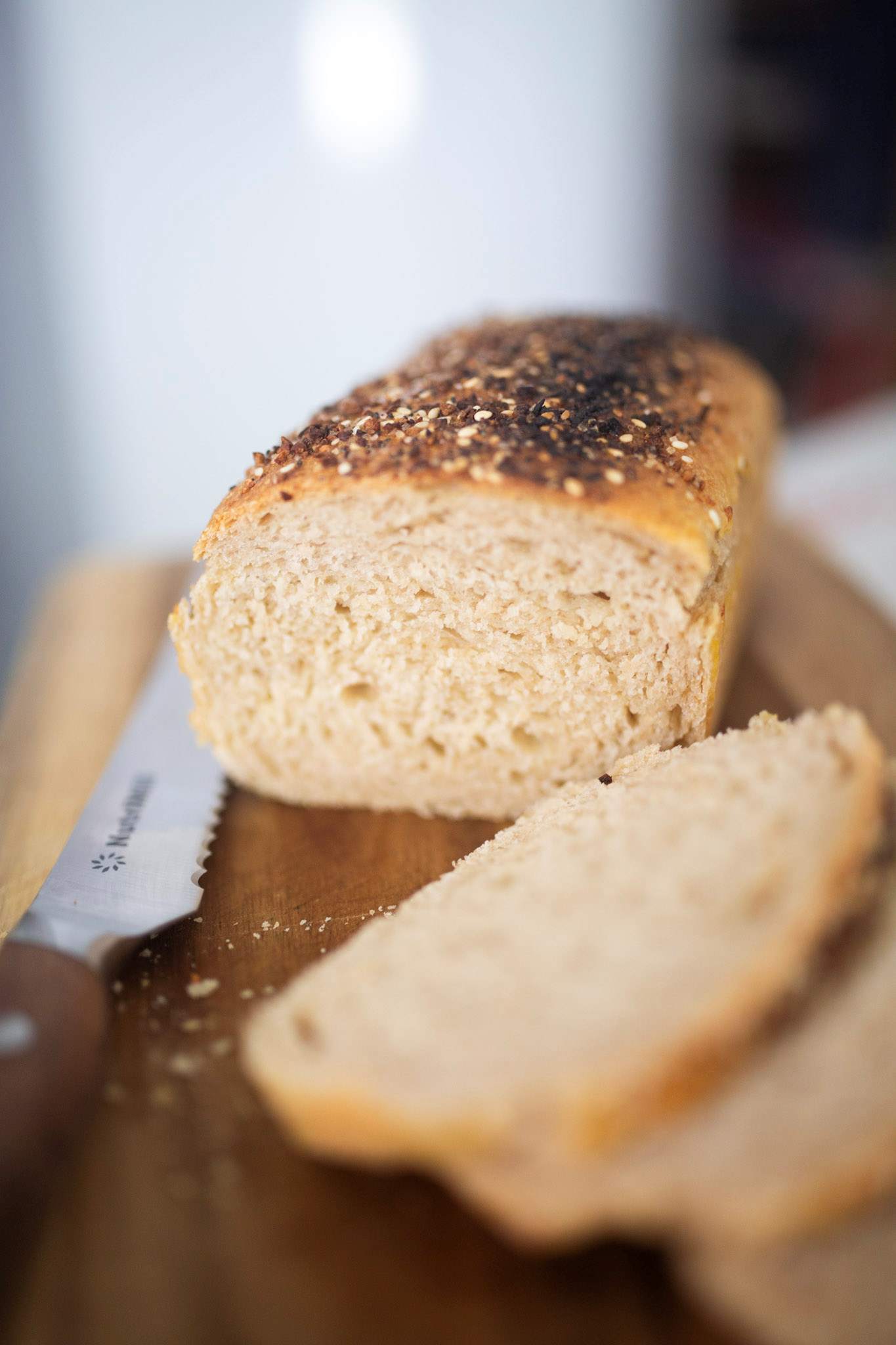 A loaf of bread topped with seeds on a cutting board with a few slices in front of it.
