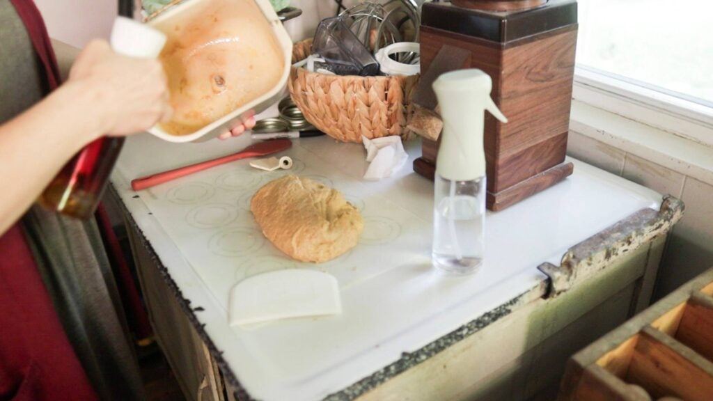 Spraying a loaf pan with oil and the dough is sitting on the counter.