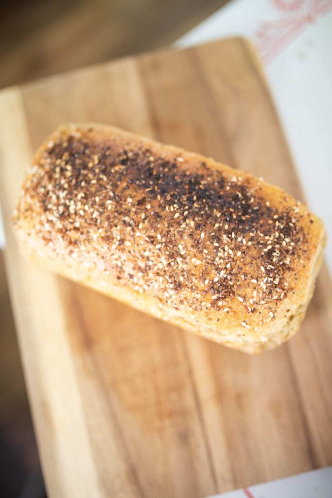 An overhead photo of a loaf of sandwich bread topped with seeds on a cutting board.