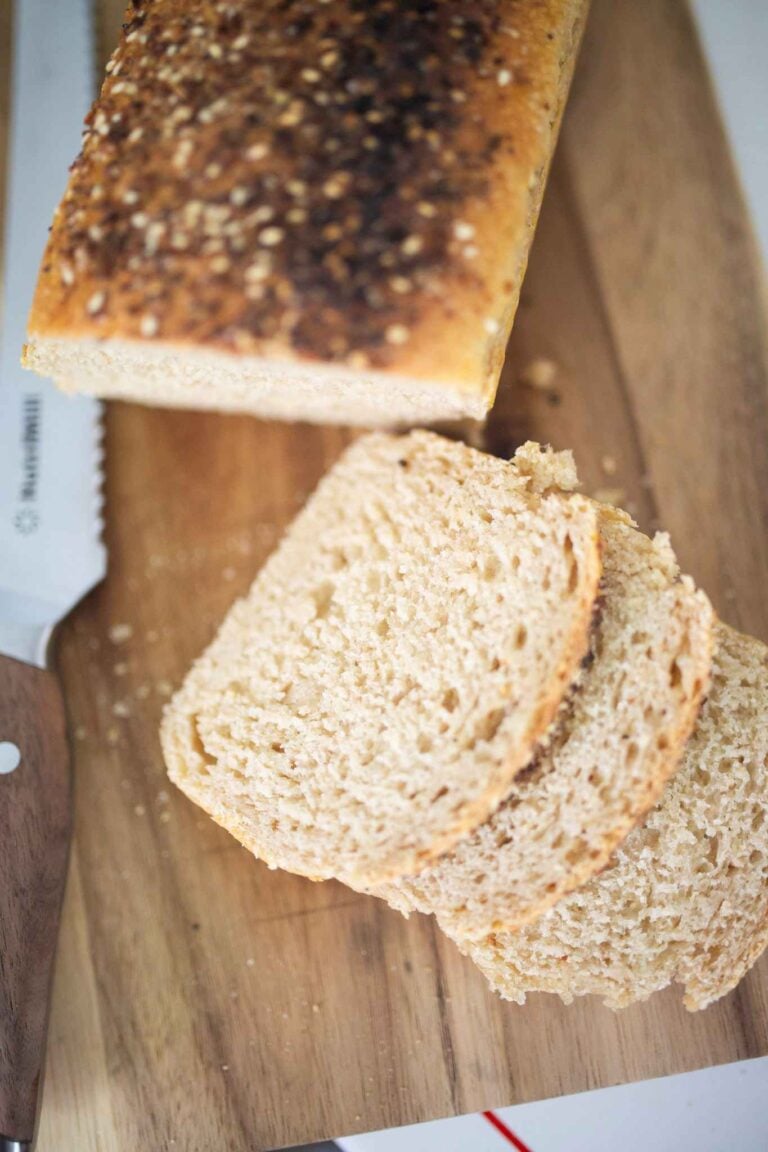 An overhead photo of a loaf of sandwich bread with 3 slices laying in front of it on a wooden board with a bread knife.