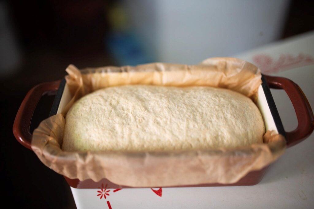 Bread dough risen in a red loaf pan with parchment paper.