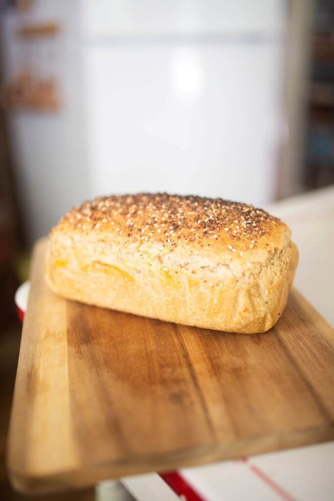 A golden brown loaf of bread on a cutting board topped with seeds.