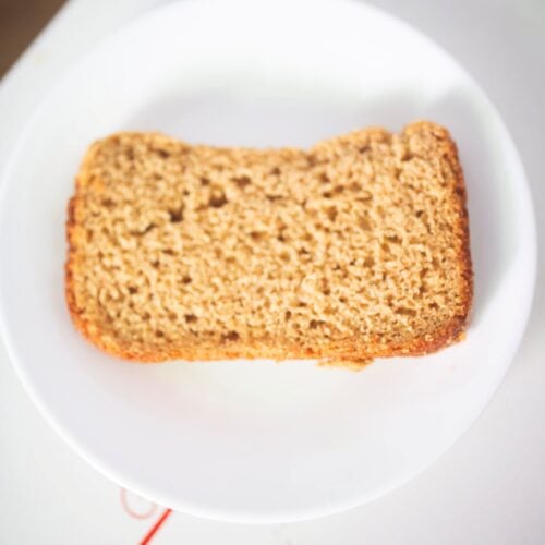 A slice of sandwich bread sits on a white plate on the kitchen table.