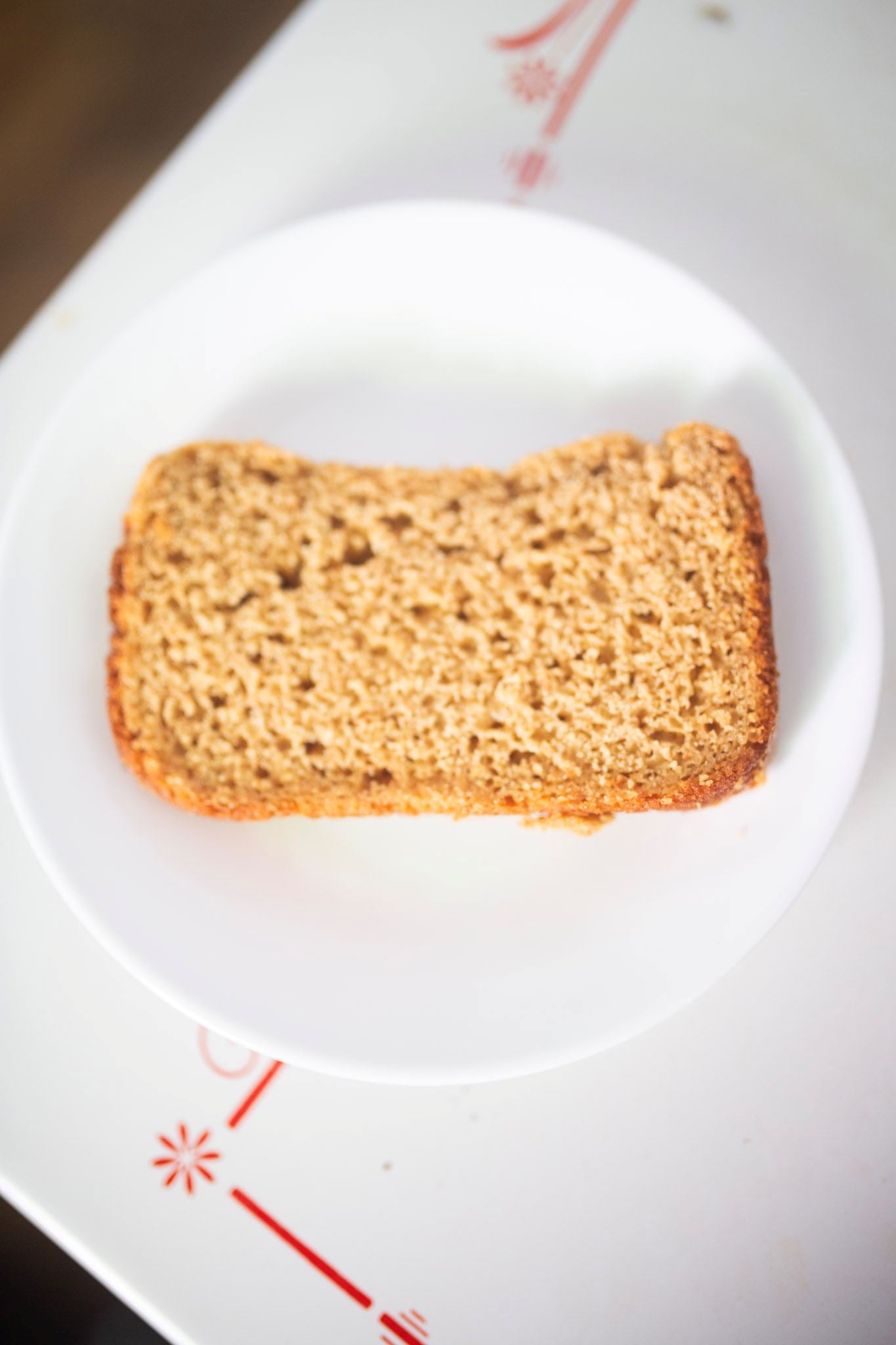A slice of sandwich bread sits on a white plate on the kitchen table.