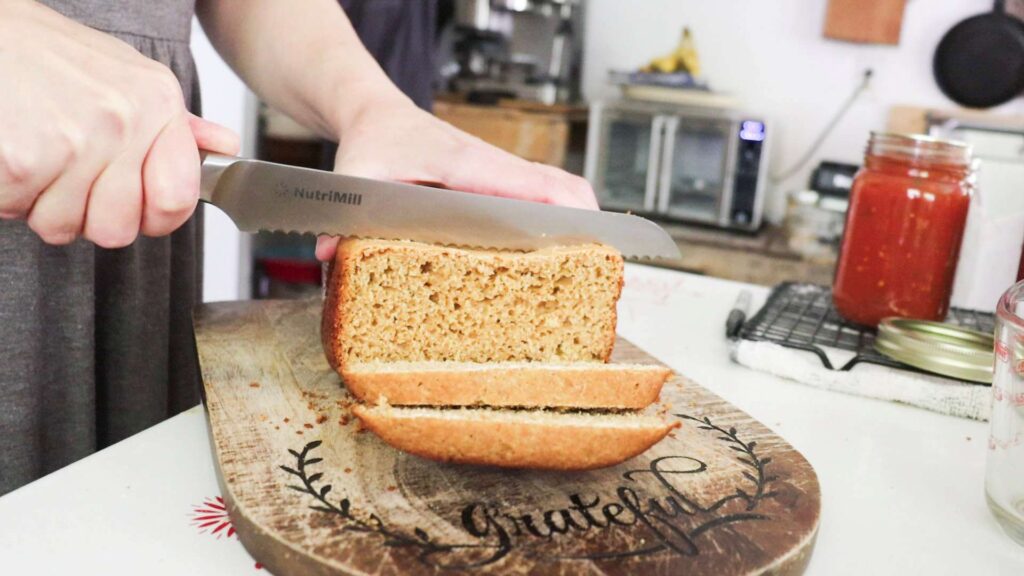 A lady is slicing a loaf of bread with a bread knife on a cutting board.