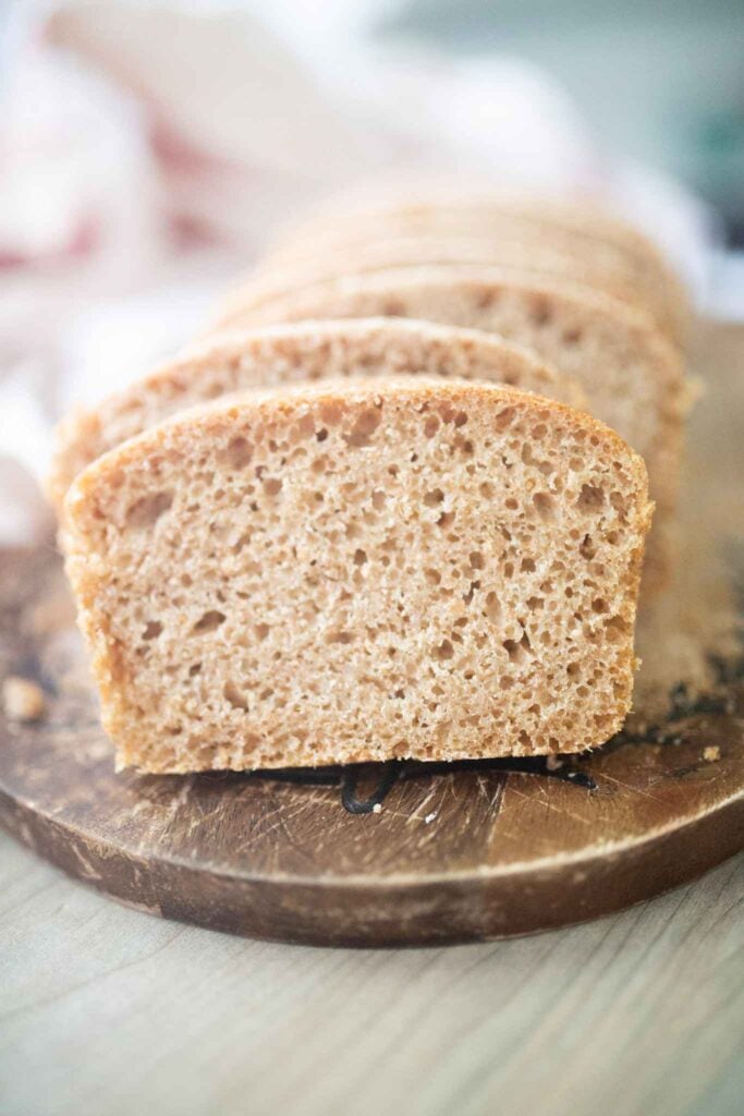 A loaf of sliced sandwich bread sits on a dark wood cutting board.