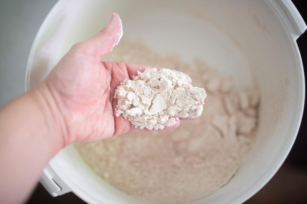 There is a hand holding flour over a big white bowl.