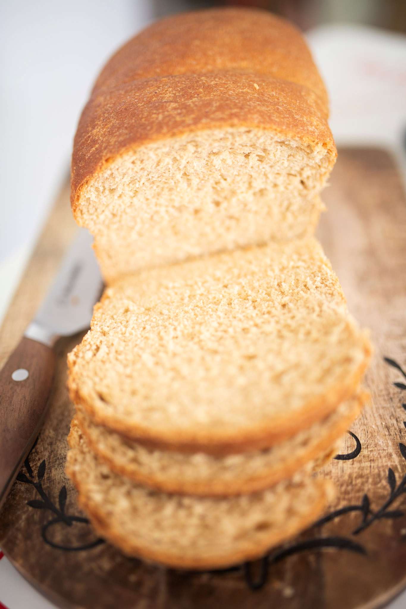 There is a sandwich loaf with a few slices on a wooden cutting board.