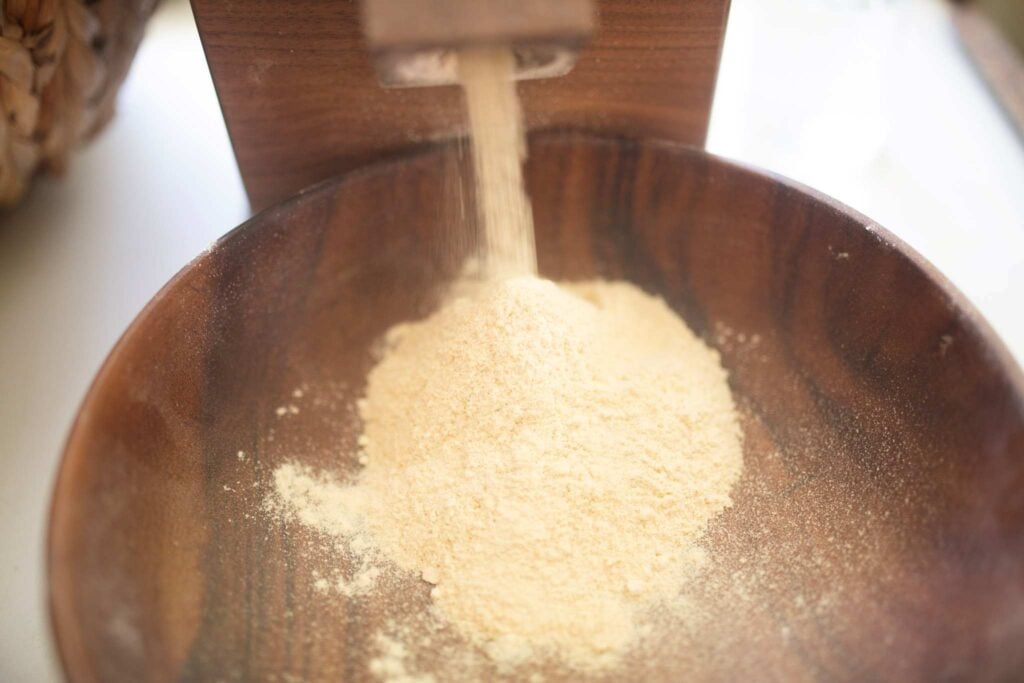 Flour is being milled from a wooden grain mill into a wooden bowl.