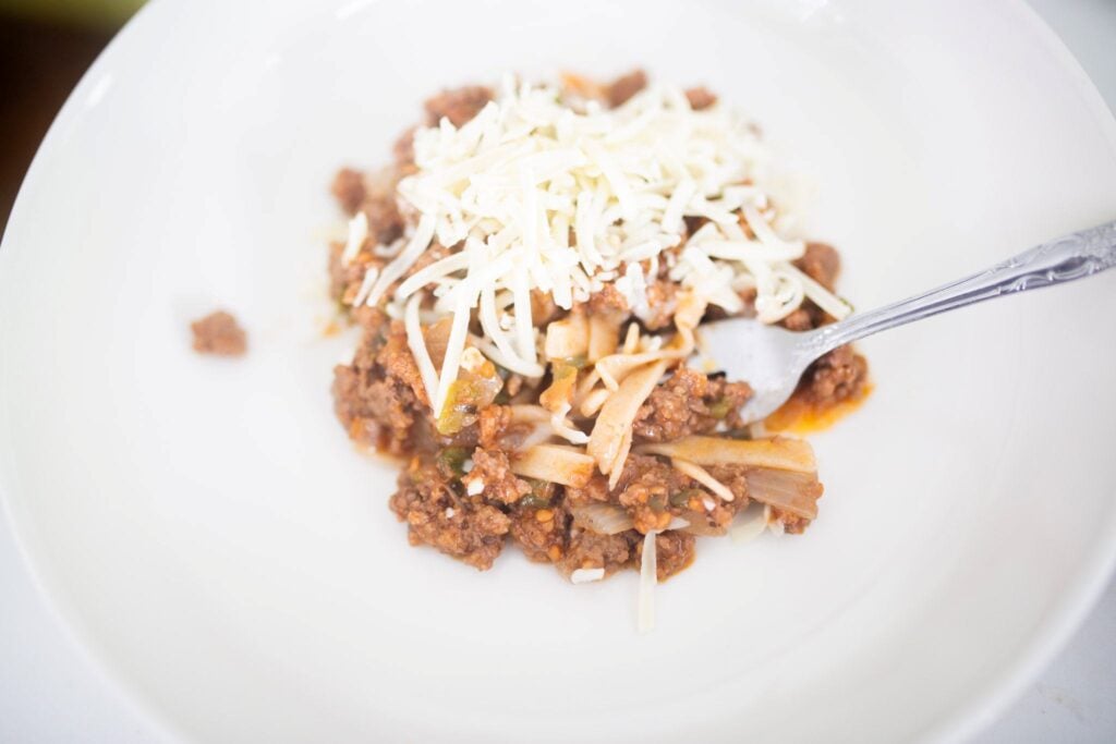 A white plate with pasta topped with meat sauce and cheese.