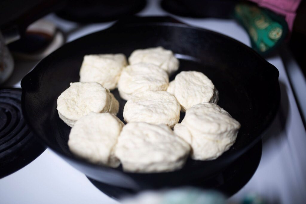 There are shaped, unbaked biscuits in a cast iron skillet.