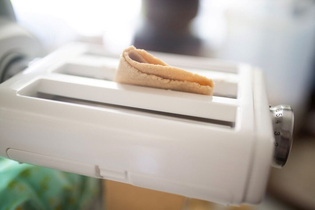 A piece of dough in being pulled through a pasta maker.