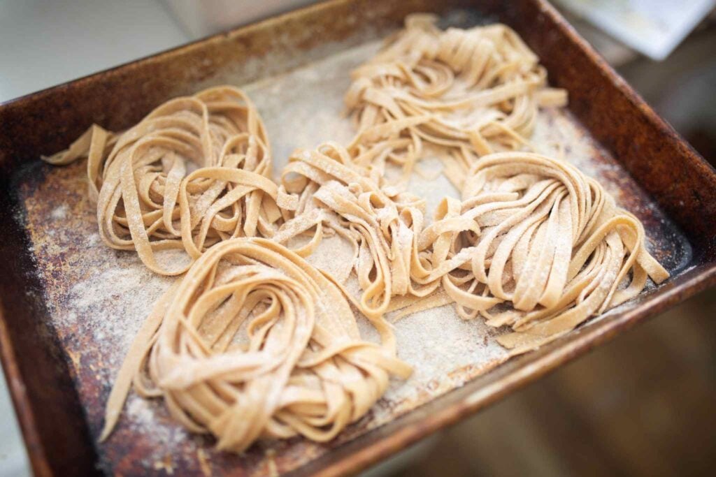 Mounds of fresh pasta noodles are laying on a floured baking sheet.