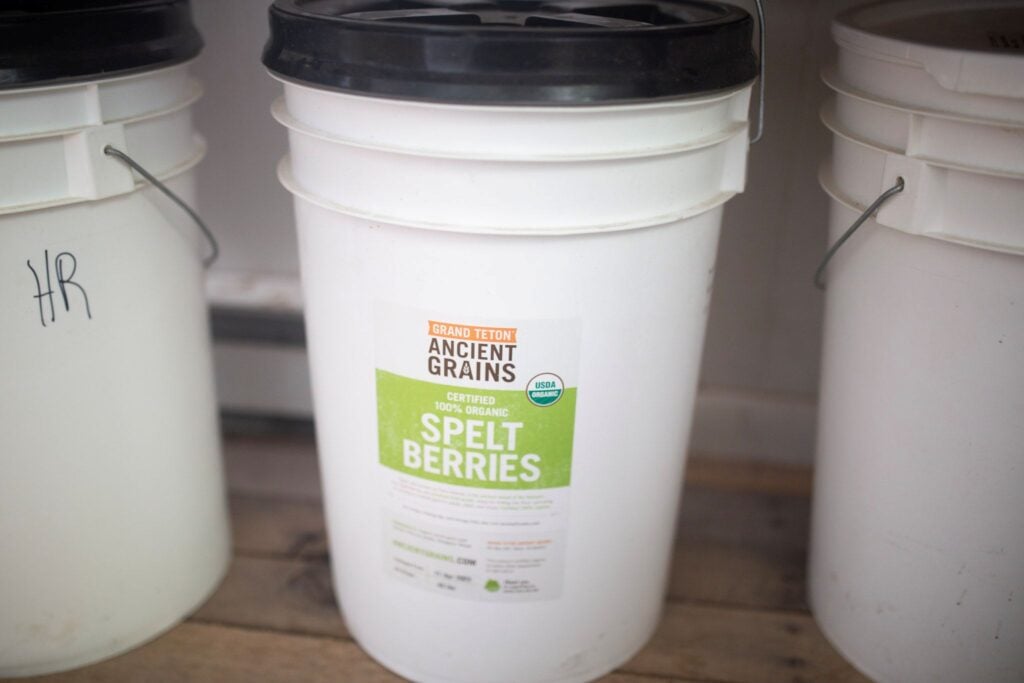 A white bucket sits on the floor with a label saying spelt berries.