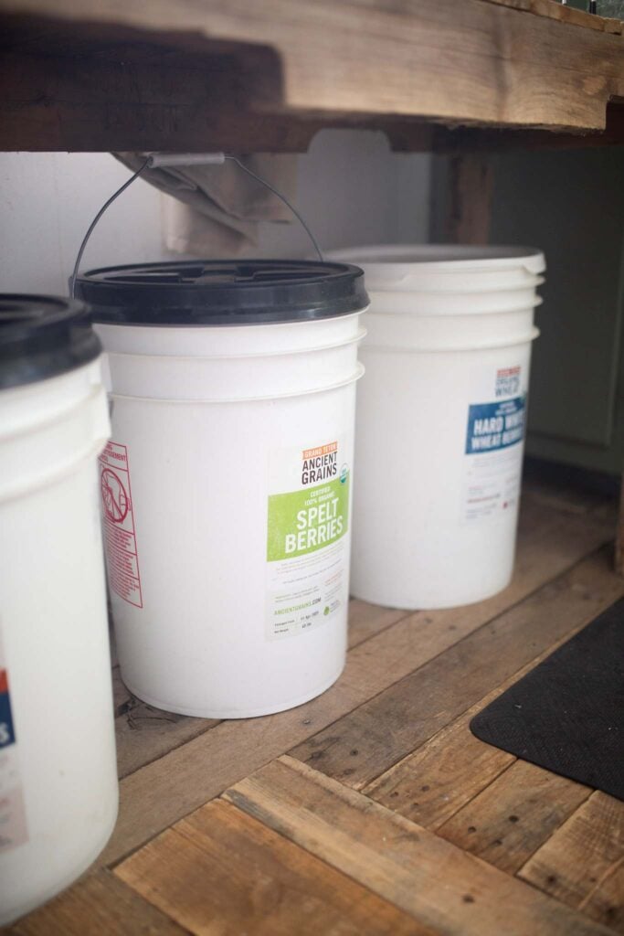 3 5 gallon buckets sitting on the floor with labels showing the type of wheat berry.