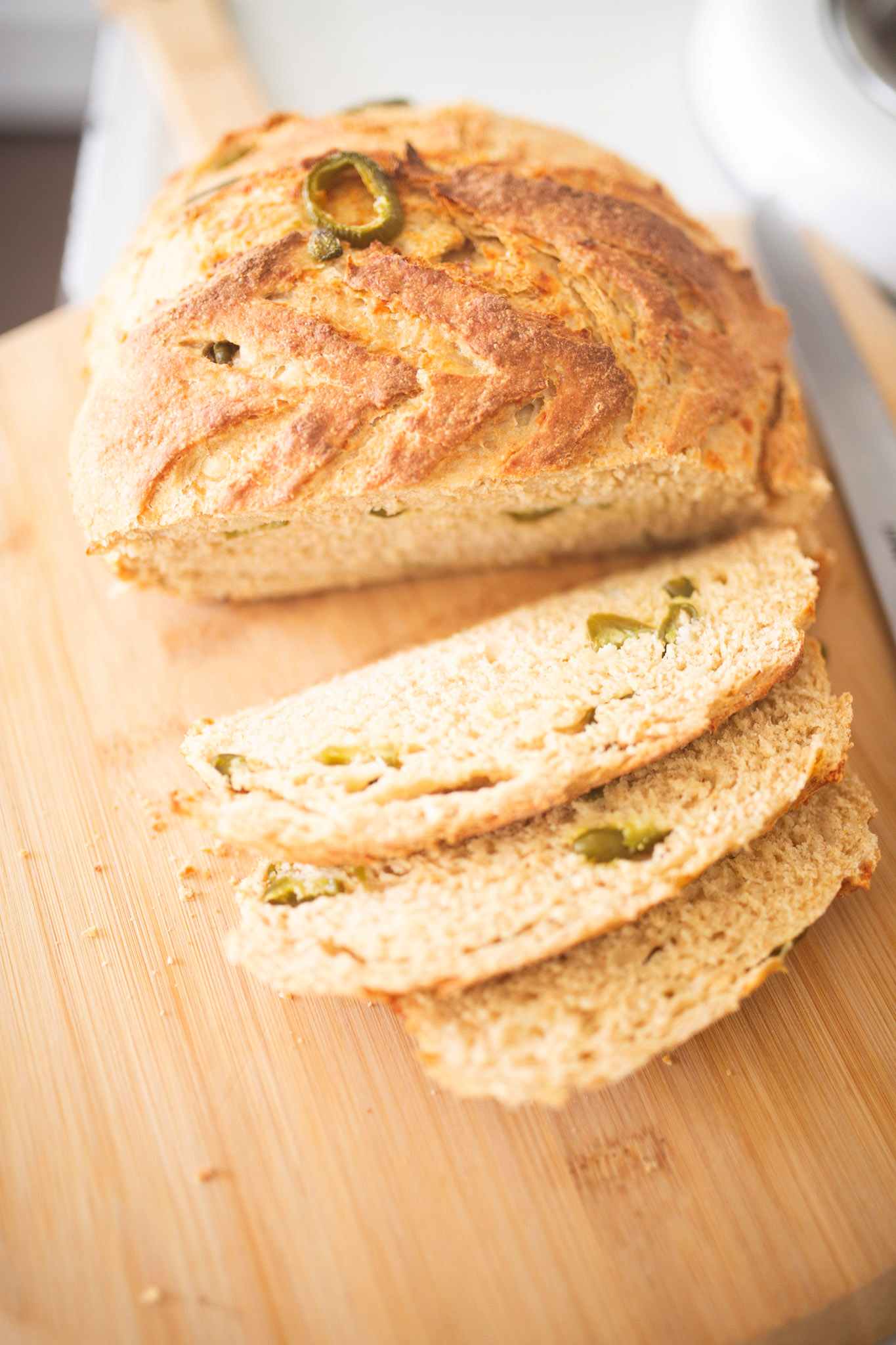 An overhead photo of an artisan loaf that has peppers showing throughout with 3 slices laying in front on a cutting board.