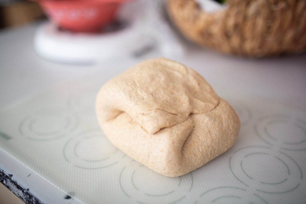 A mound of bread dough is folded on itself sitting on a silicone dough mat.