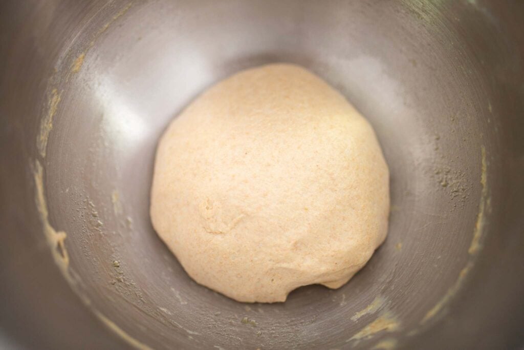 A ball of bread dough sits in a stainless steel bowl.
