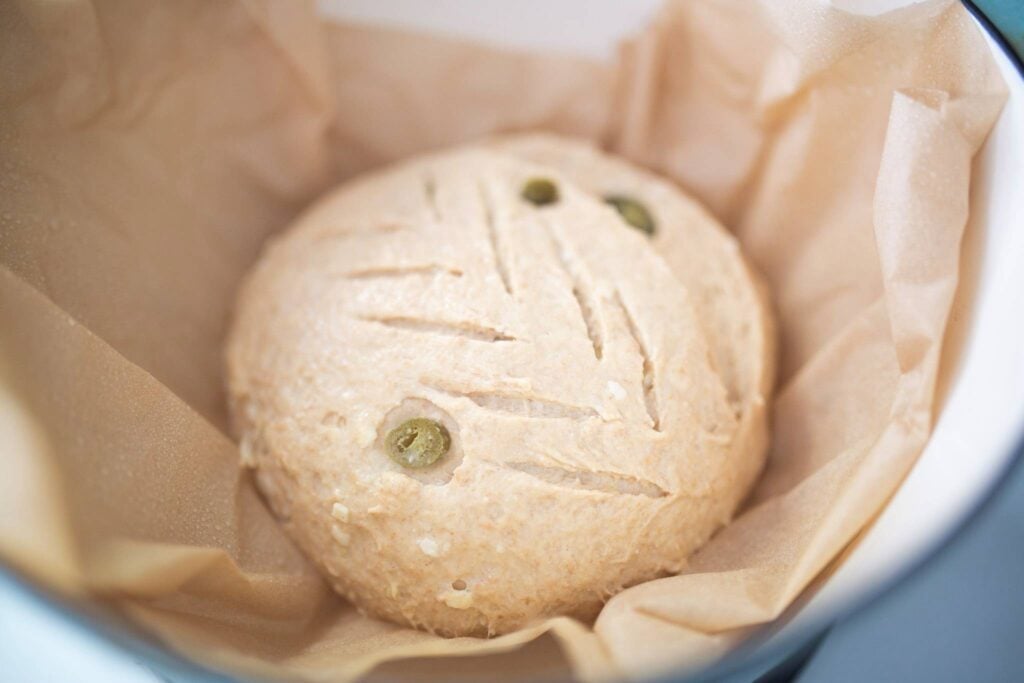 Scored dough sits in a pot sprayed with water. It is scored across the top.
