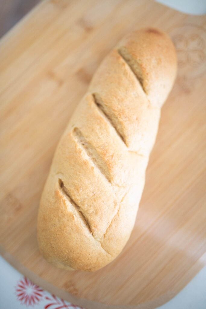 This is a large loaf of submarine sandwich bread on a cutting board. It is scored diagonally across the top.
