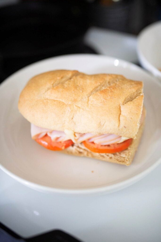 This is a submarine sandwich with tomatoes showing and deli meat sitting on a white plate.