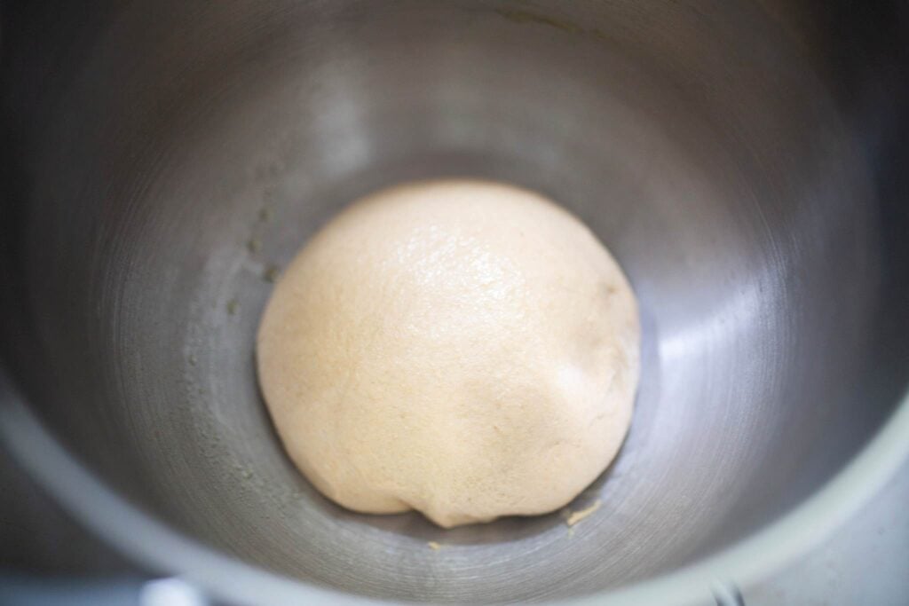 A ball of dough is in a stainless steel bowl.