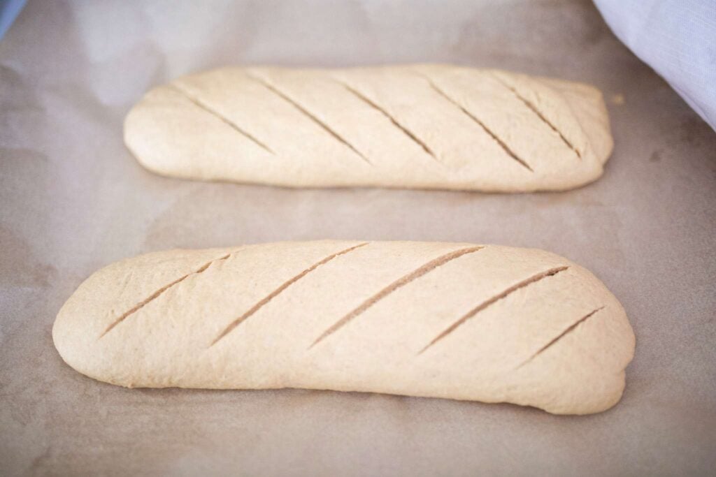 2 shaped logs of dough scored diagonally across the top on a piece of parchment paper.