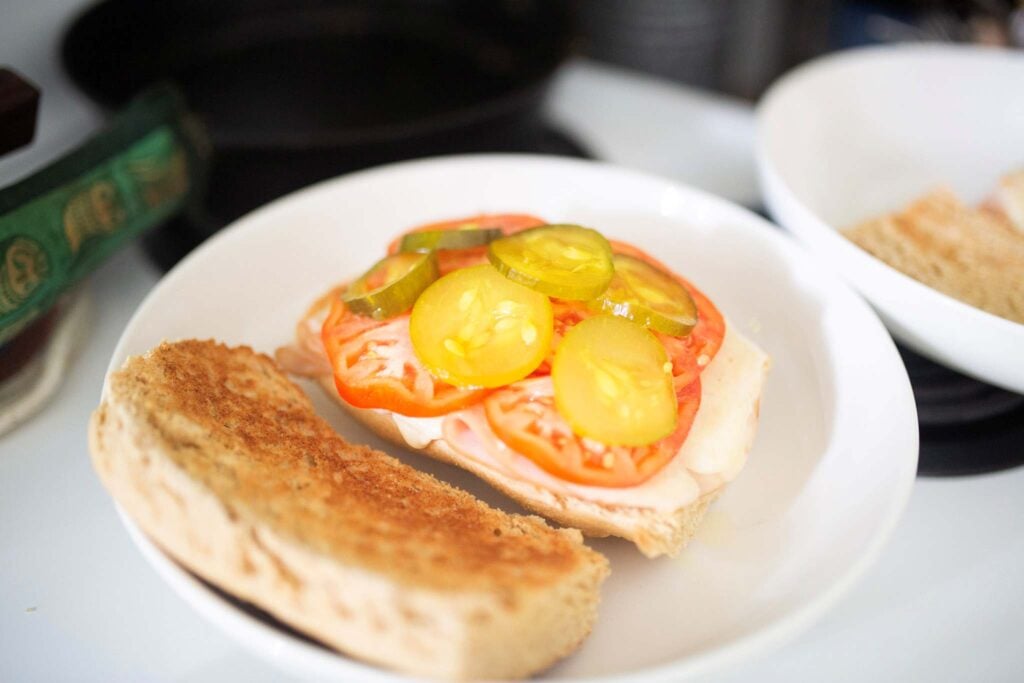 This is an open faced submarine sandwich topped with tomatoes and pickles.