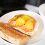 This is an open faced submarine sandwich topped with tomatoes and pickles.