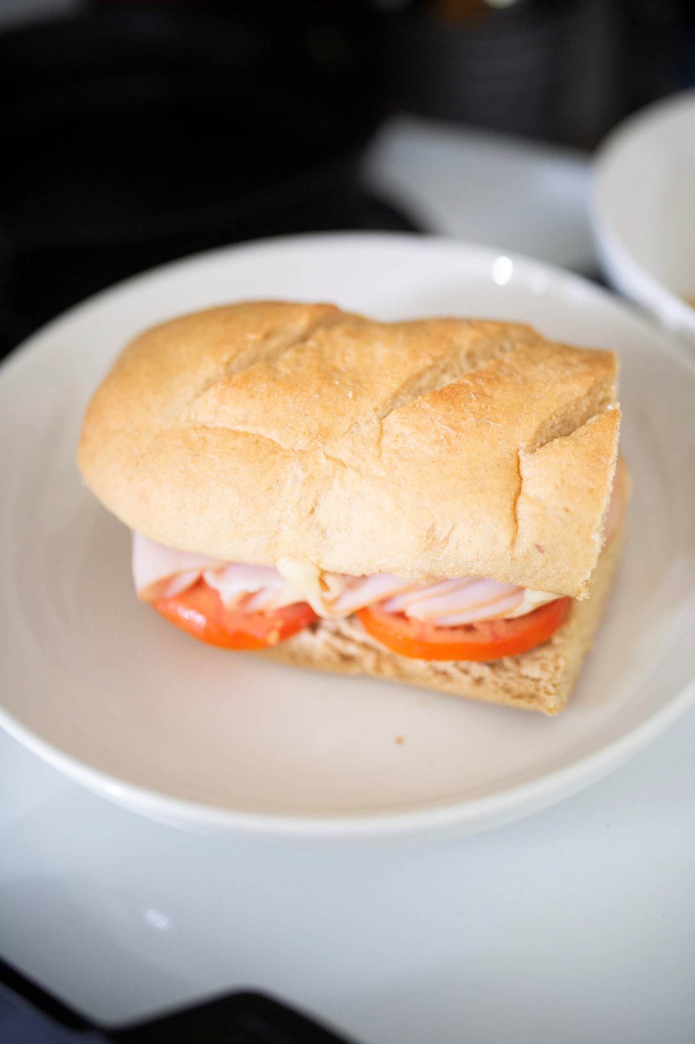 This is a submarine sandwich with tomatoes showing and deli meat sitting on a white plate.