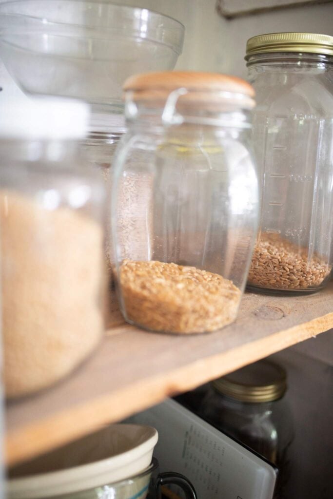 Several different sized jars full of whole grains on a shelf.
