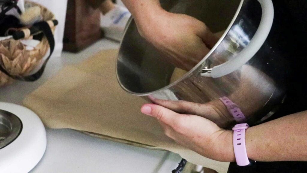 A hand is punching down into a stainless steel bowl.