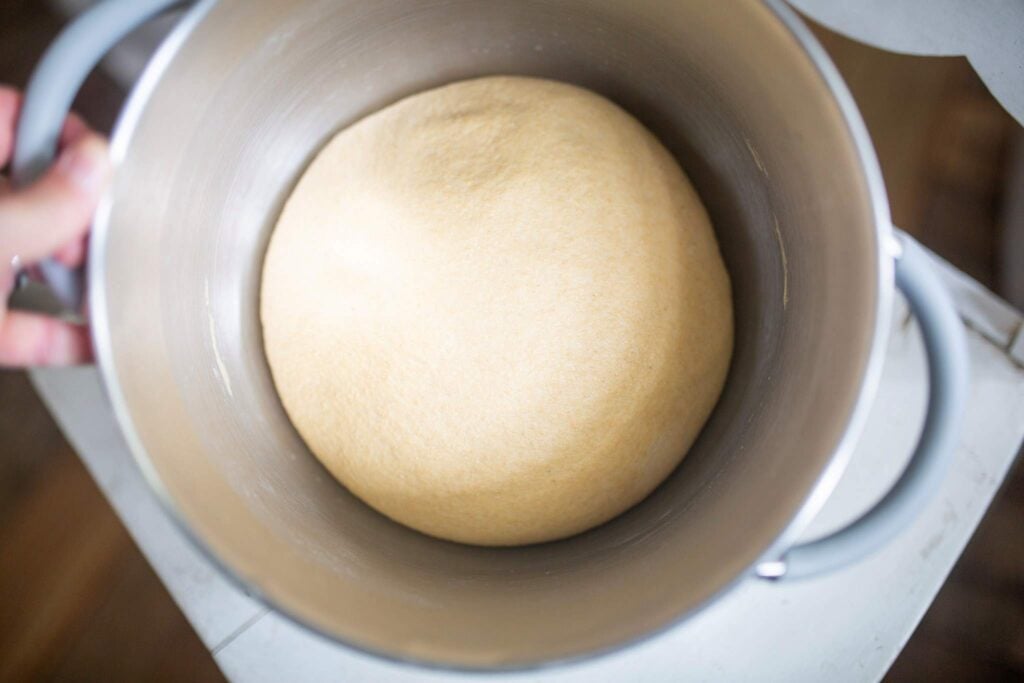 A risen ball of dough in a stainless steel bowl.