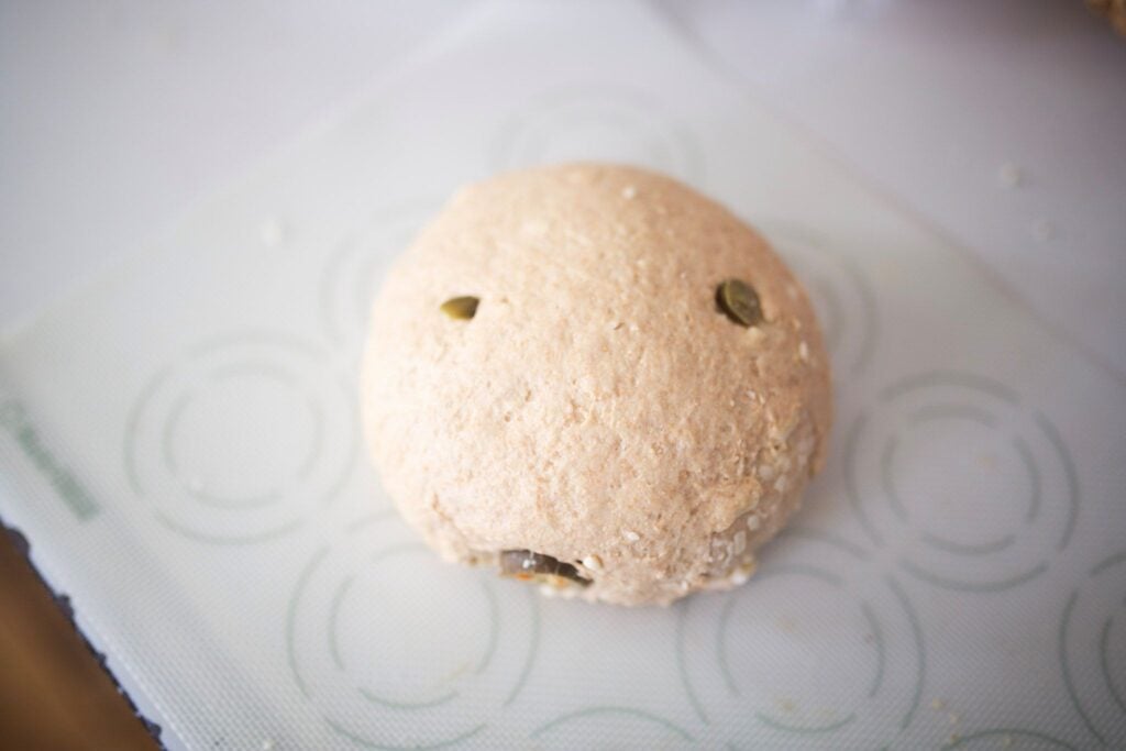 A ball of bread dough with jalapenos showing in the dough sits on a silicone dough mat.